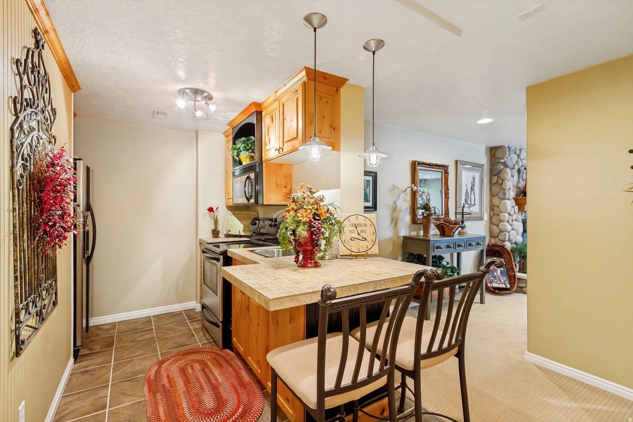 Compact kitchen area featuring wood cabinetry, stainless steel appliances, a breakfast bar with pendant lighting, and tile flooring