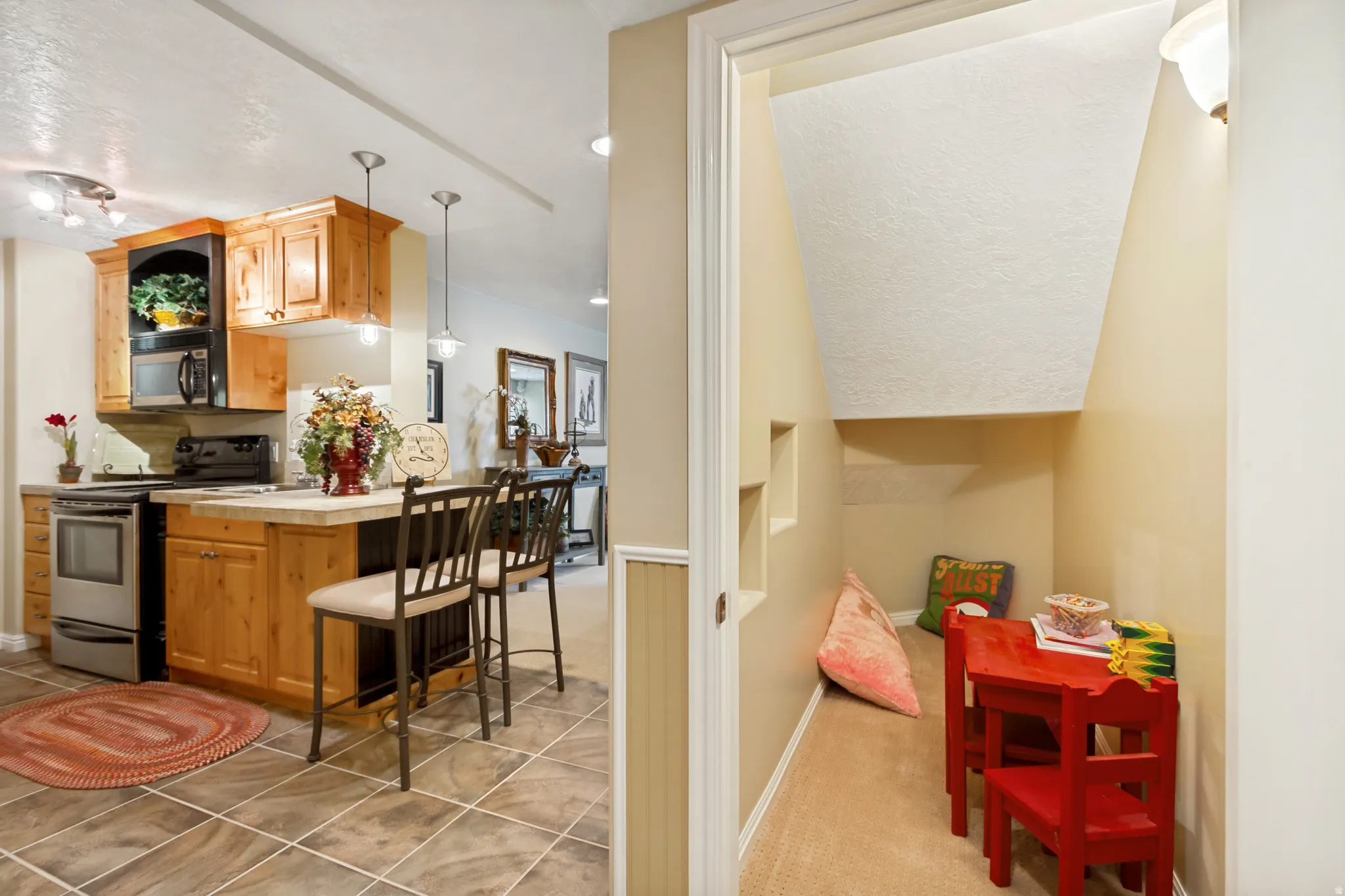 Compact kitchen featuring wood cabinetry, stainless steel range and microwave, a peninsula with seating, and ceramic tile flooring