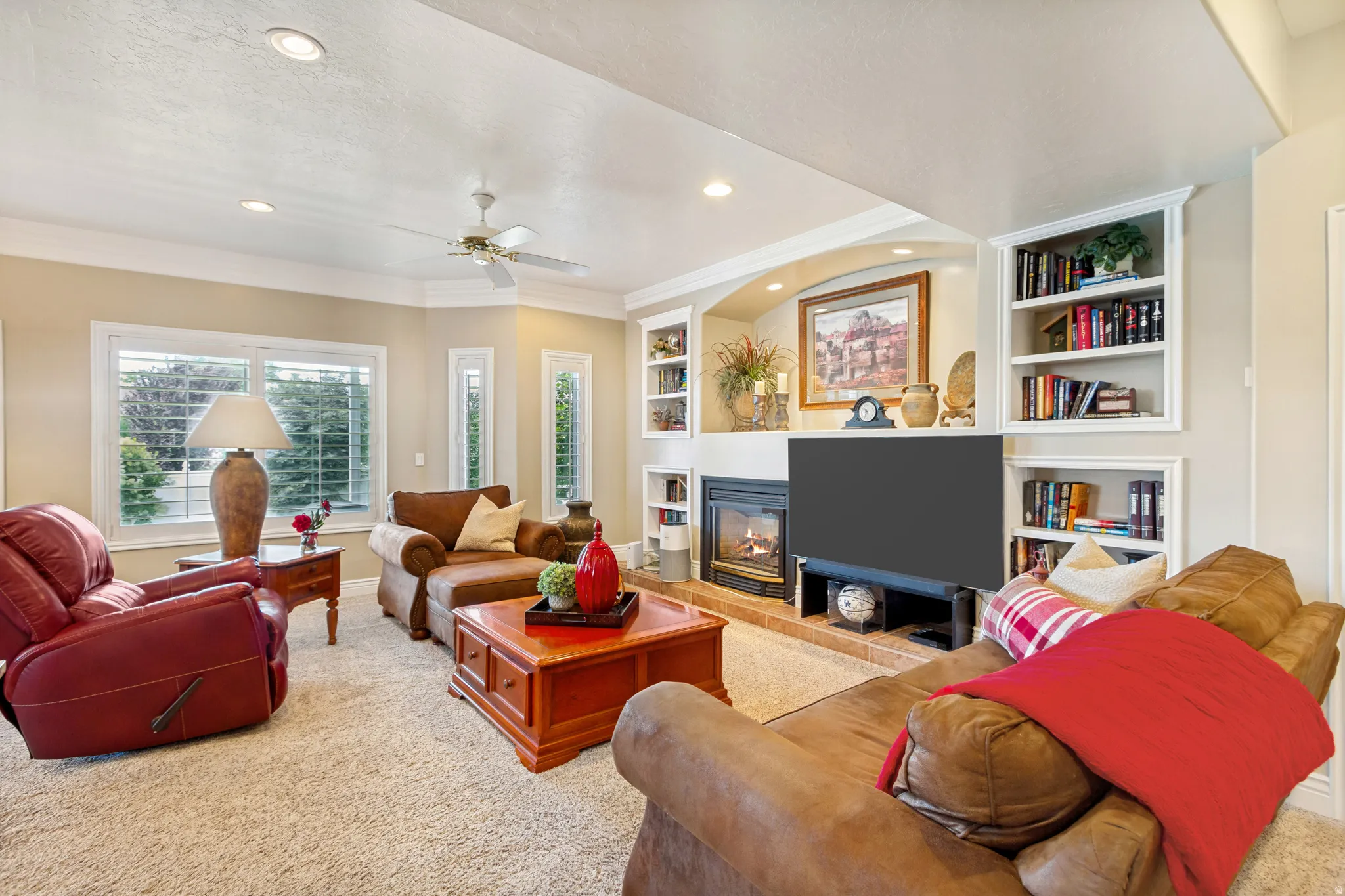 Living area featuring a gas fireplace with a raised hearth, built-in shelving, recessed lighting, and a ceiling fan