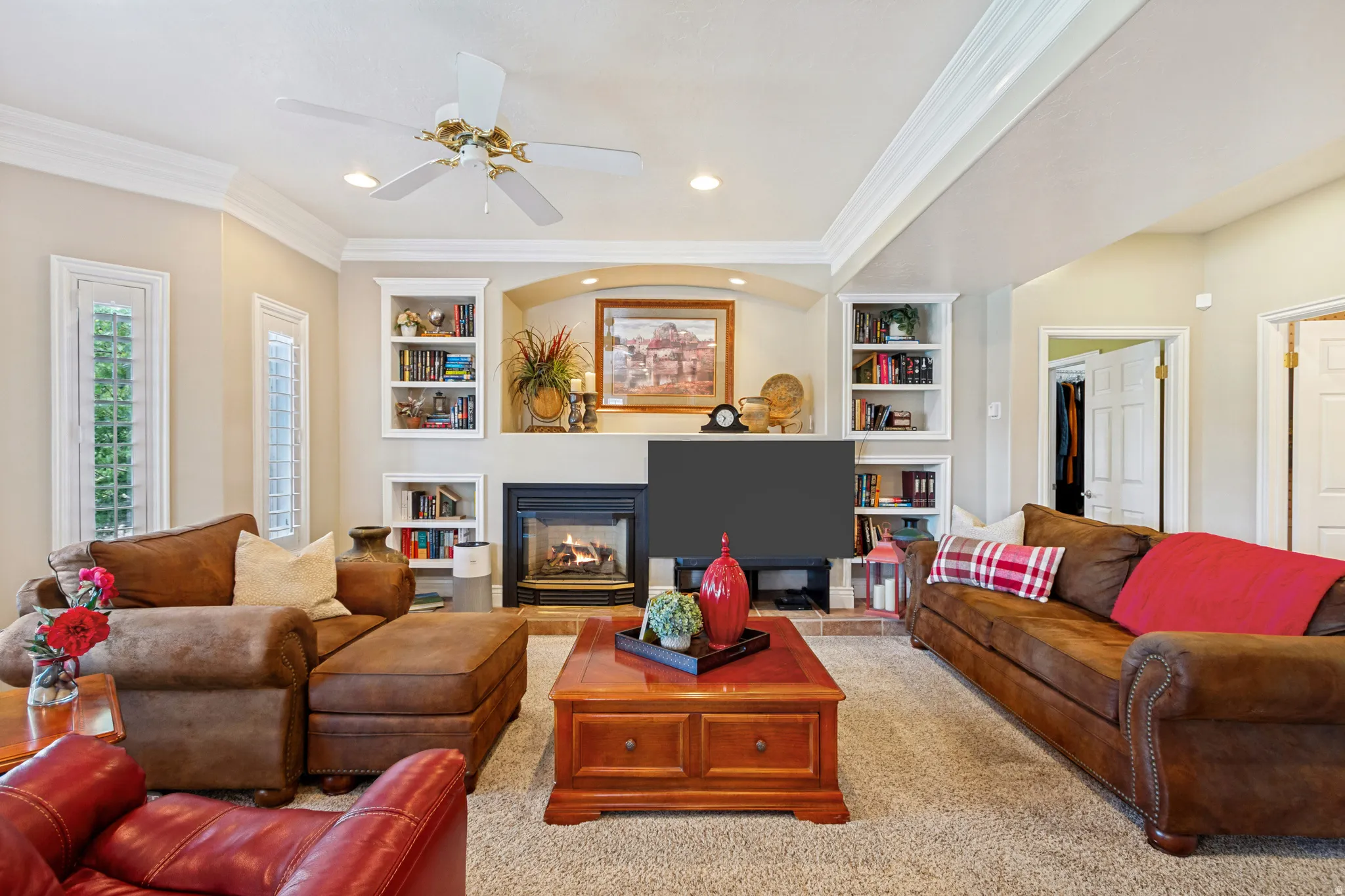 Living area featuring a fireplace with a dark surround, built-in shelving, tray ceiling, recessed lighting, and a ceiling fan