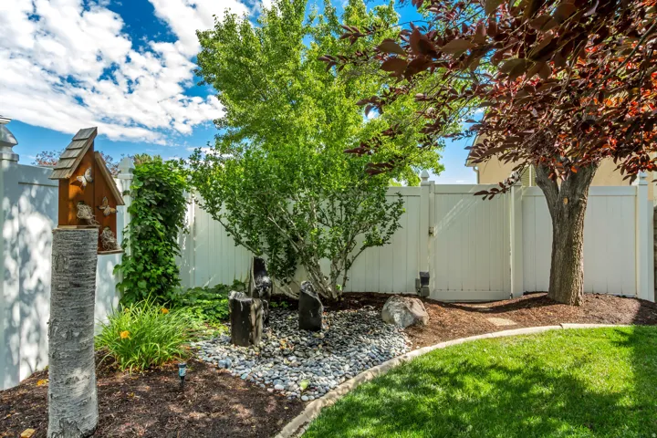Manicured lawn area with a white privacy fence, mature trees, and decorative rock landscaping