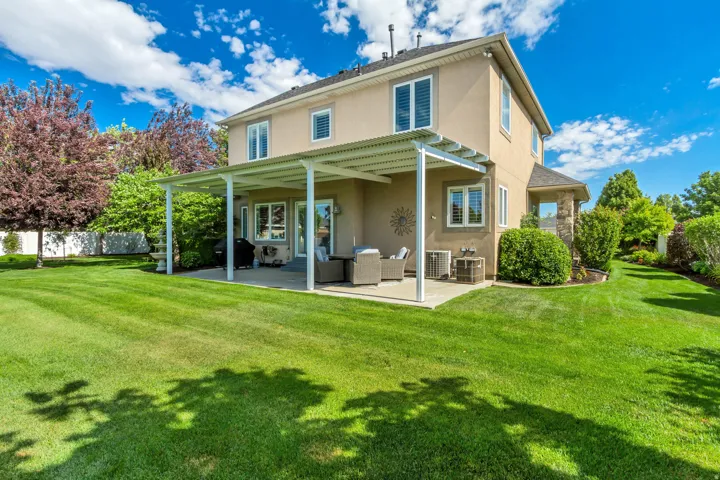 Expansive rear yard featuring a large concrete patio with a white metal pergola