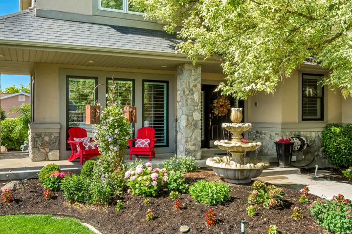 Front exterior featuring a covered porch, stone facade accents, mature landscaping, a multi-tiered water fountain, and a dark entry door