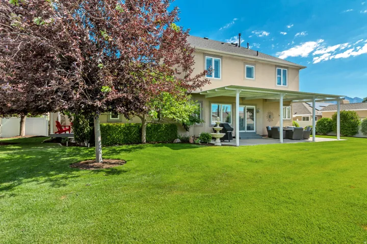 Expansive backyard featuring a large green lawn, mature trees, a covered patio structure, and a concrete patio