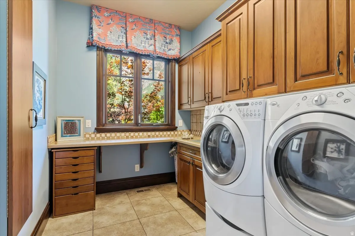 Dedicated utility room featuring abundant wood cabinetry, a built-in countertop, a window with natural light, and tile flooring. One of two laundry rooms