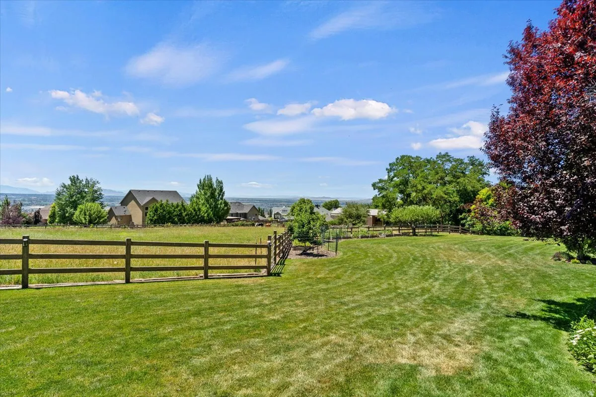 Expansive lawn area with a three-rail fence, mature trees, and landscaping, set against a distant mountain backdrop