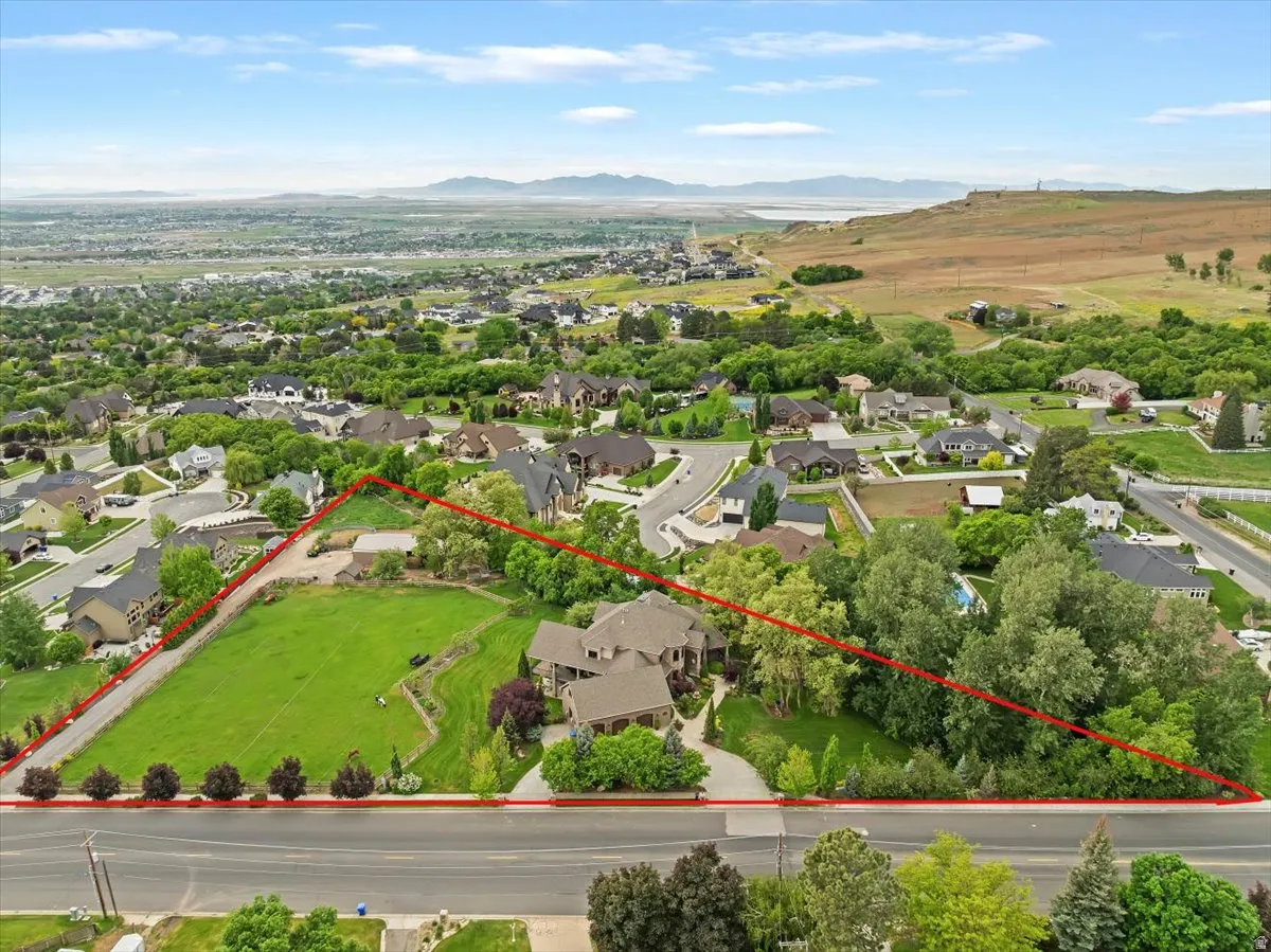 Rare 3 acre property featuring a substantial green space, mature trees, paved driveways, a large residential structure with a multi-gabled roof, and a distant mountain range