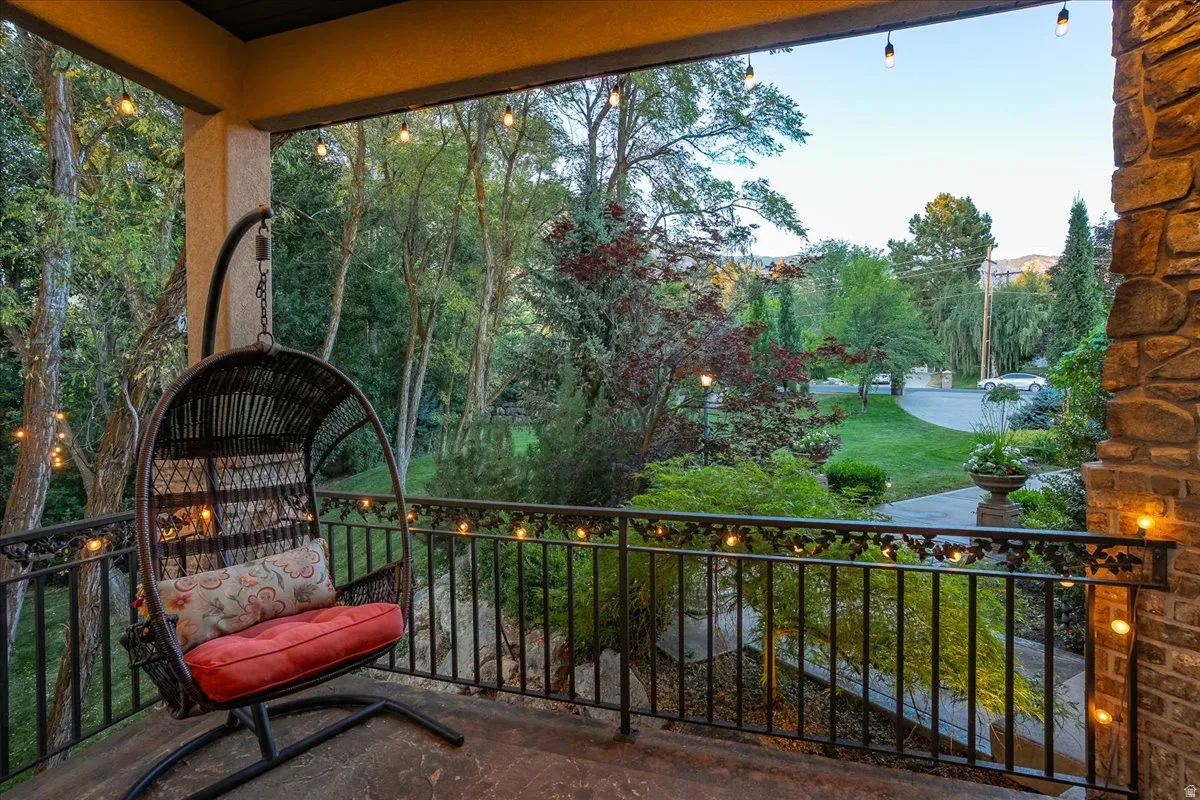 Covered balcony featuring a decorative wrought iron railing, string lighting, and a stone-clad exterior wall