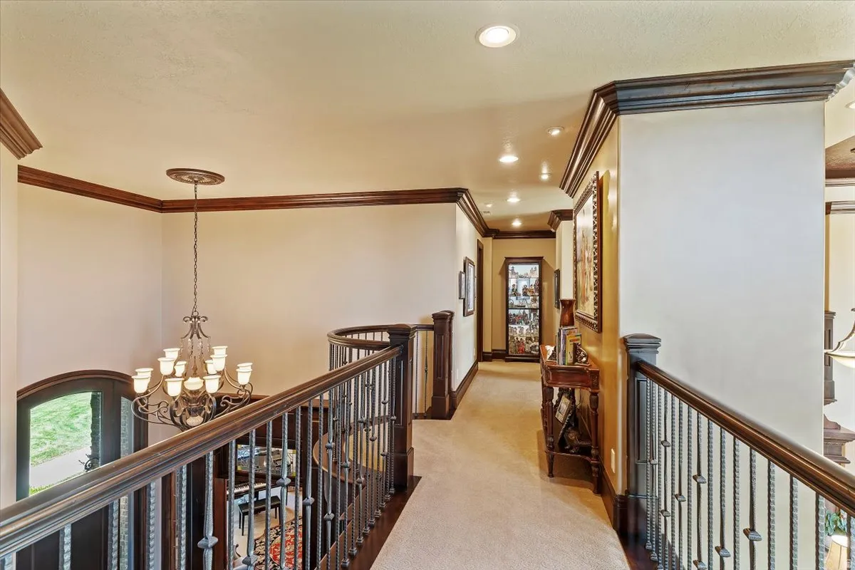 Upper-level hallway featuring dark wood crown molding, a wrought iron and wood banister, recessed lighting, and beige carpeting