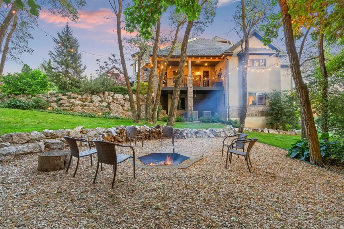 Expansive backyard featuring a gravel fire pit area with a stone retaining wall, mature trees, and string lighting