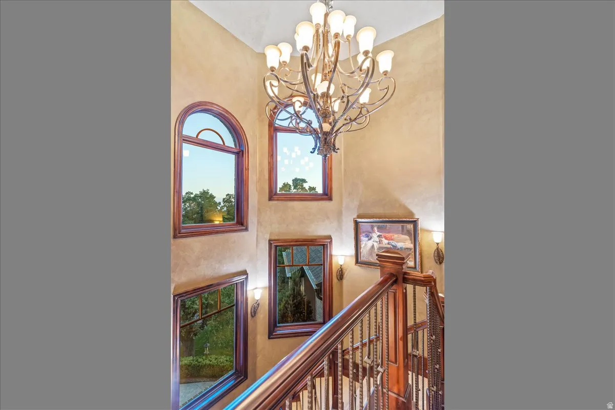 Architectural staircase featuring a wrought iron chandelier, multiple arched and rectangular windows with wood framing, and wood handrails with decorative balusters