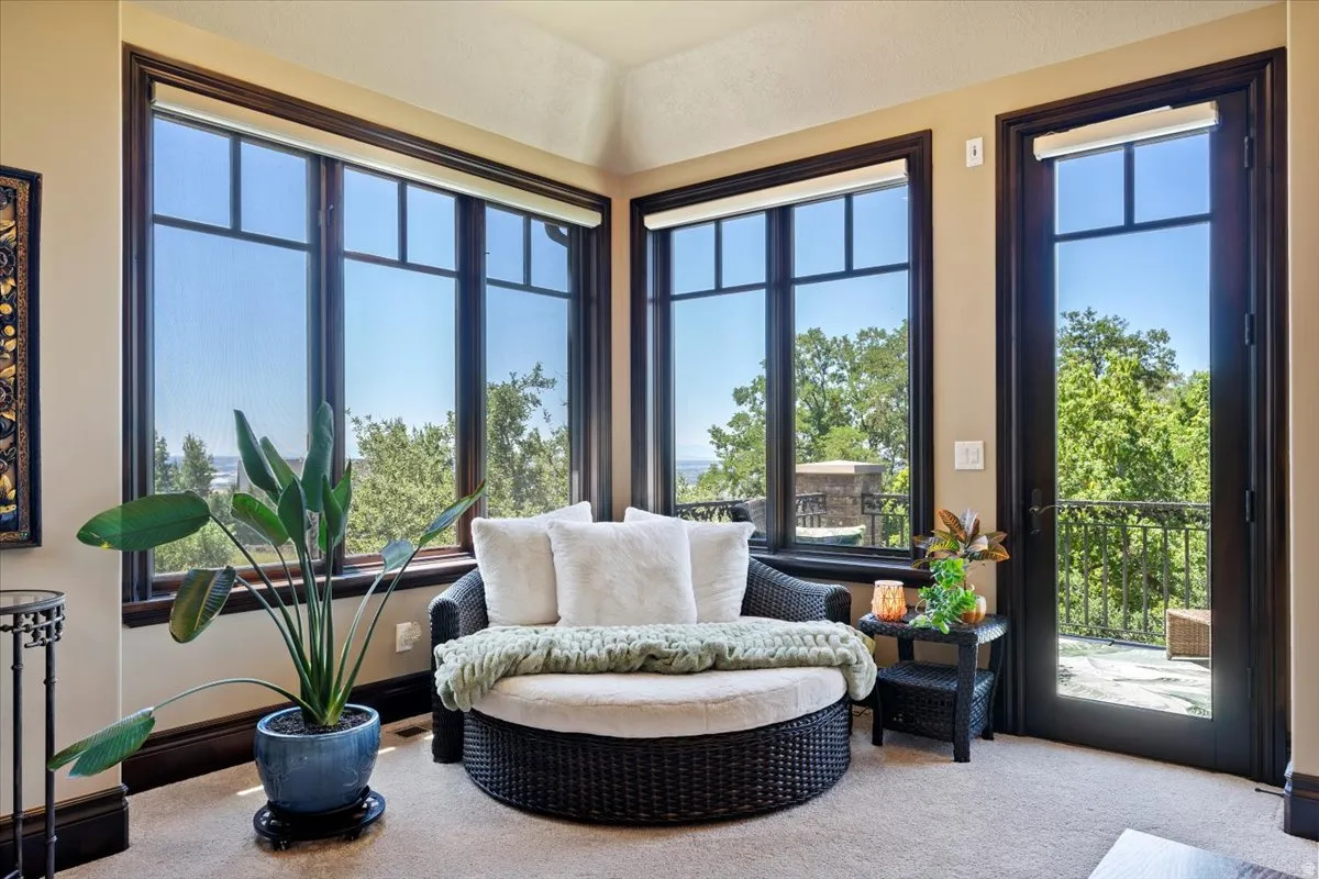 Corner room featuring multiple large windows with dark trim, a matching glass-panel door, and access to an exterior balcony with wrought iron railing