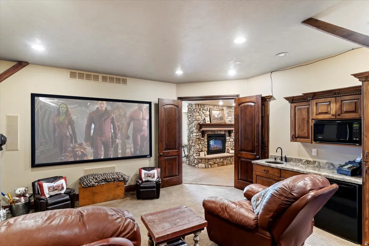 Entertainment area with a large projector screen, built-in cabinetry, an under-counter refrigerator, a compact microwave, and a wet bar with a dark faucet