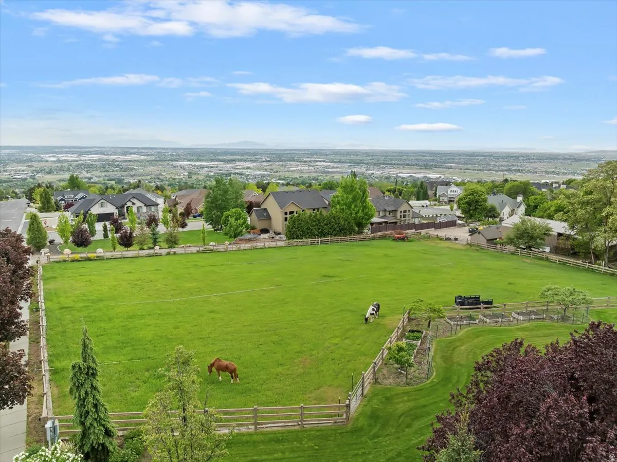 Expansive green pasture with wood fencing, mature trees, and garden beds