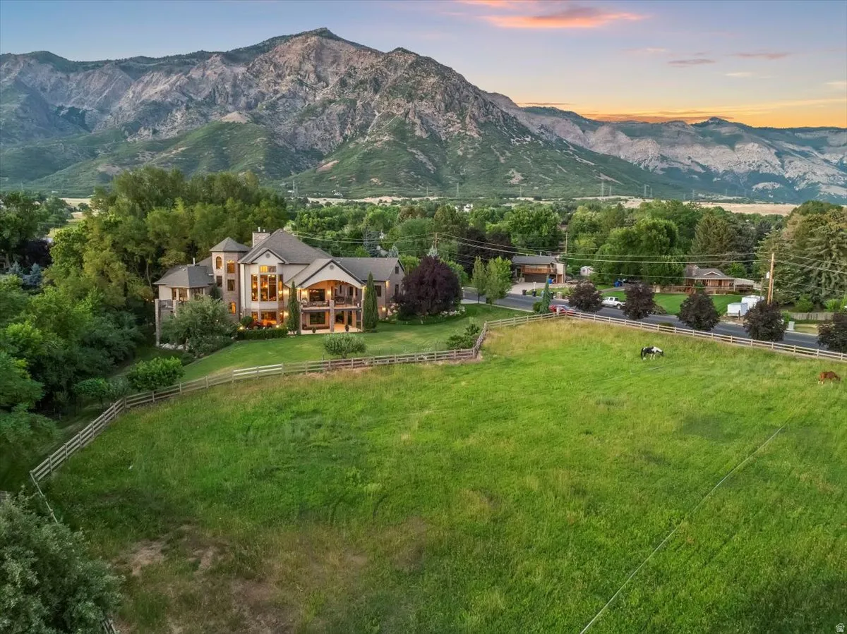 Expansive green acreage with a four-rail fence and a stunning mountain backdrop