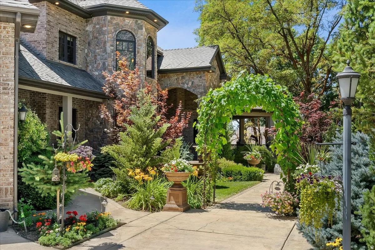 Stone and brick exterior with arched windows, a covered entryway, and a vine-covered archway over a paved path