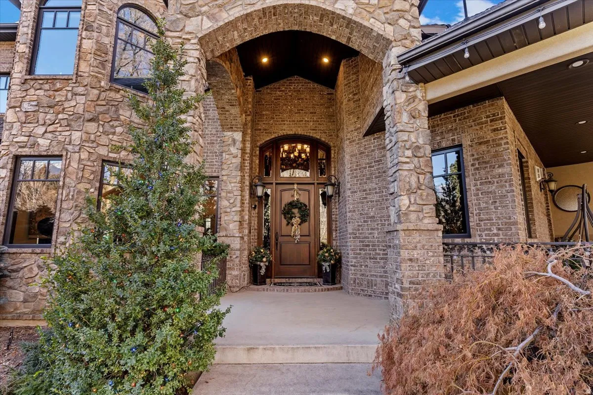 Entry featuring an arched entryway,  distinguished dark wood front door with arched glass panels, and a covered porch with a iron