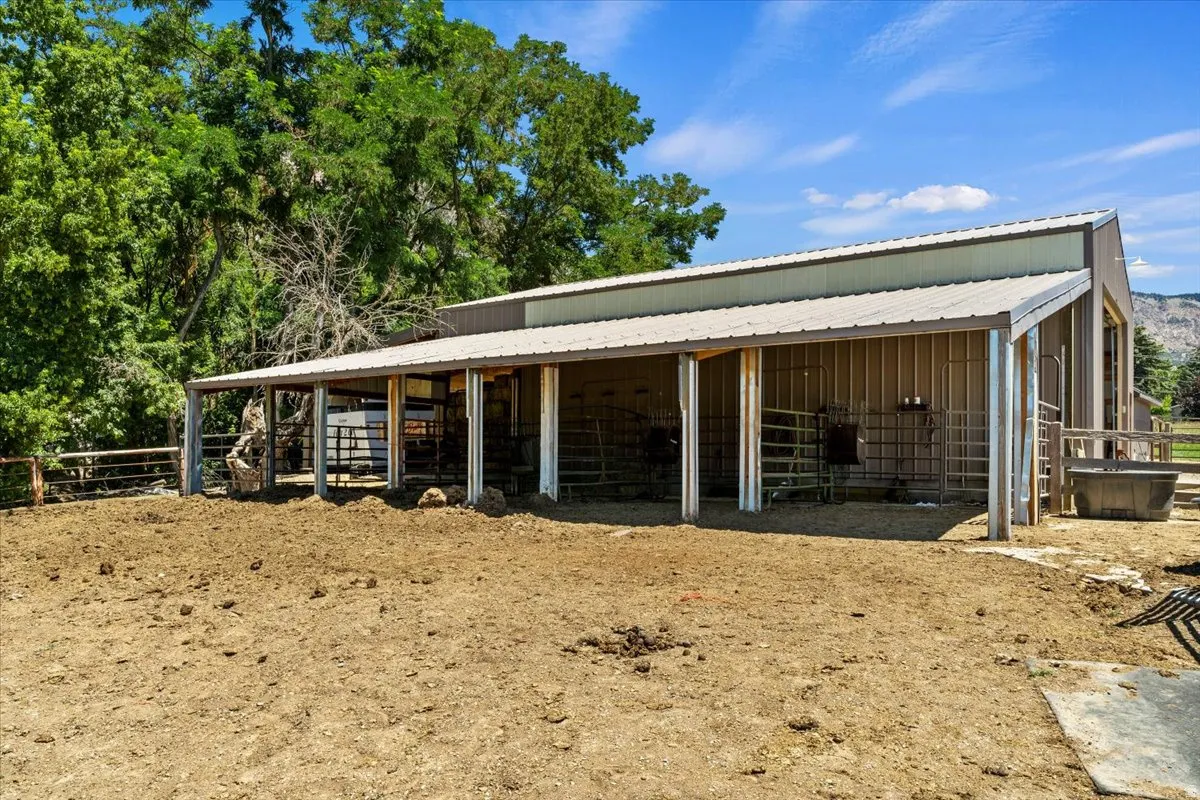 Metal-clad barn structure featuring multiple covered stalls, a durable corrugated metal roof, and an expansive dirt paddock