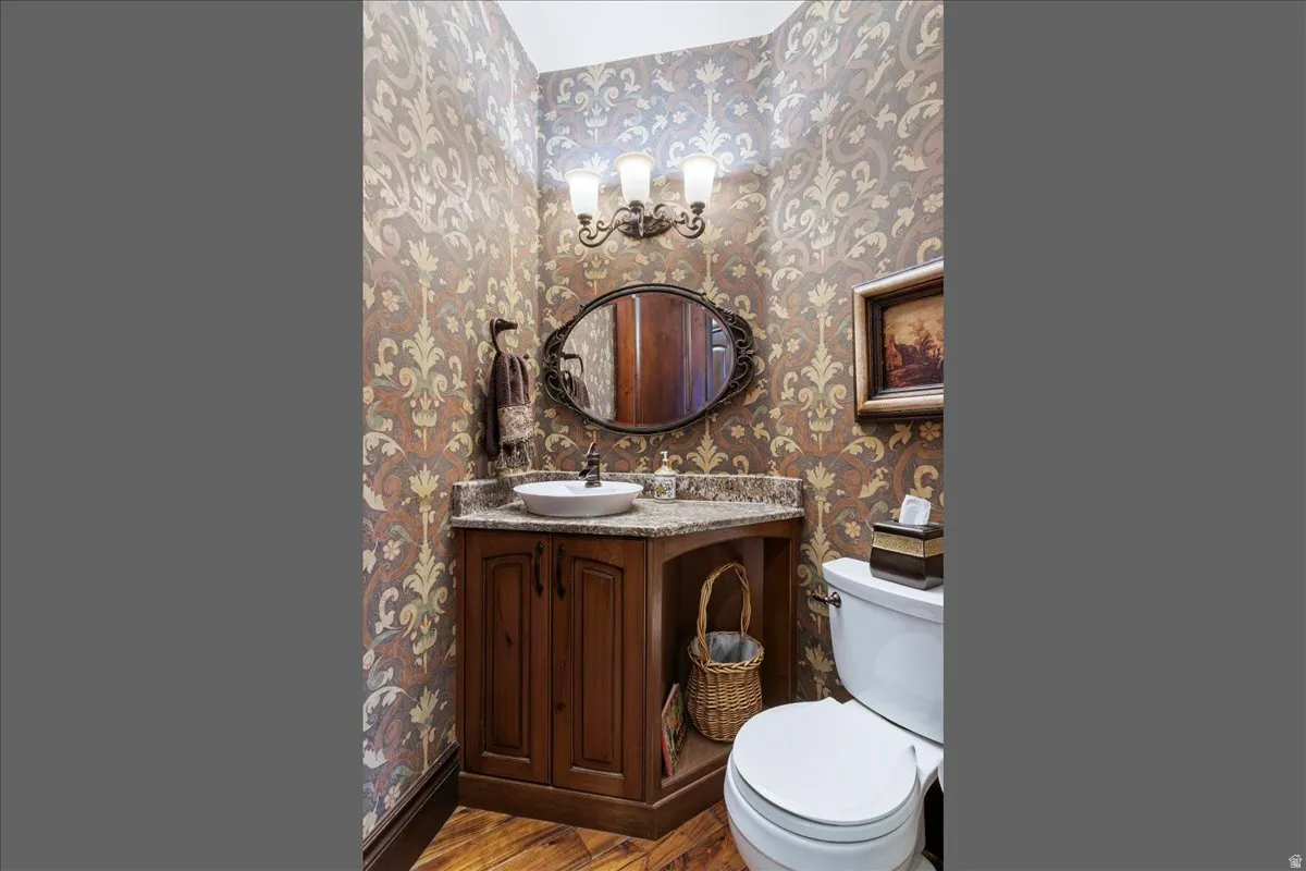Powder room featuring ornamental wallpaper, a wood vanity with a vessel sink, a stone countertop, and a decorative mirror