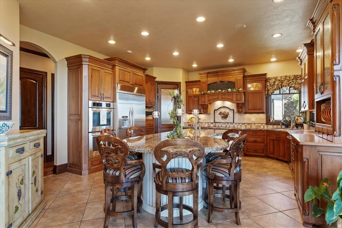 Expansive kitchen featuring an oversized island with seating, integrated stainless steel appliances, custom cabinetry, a tile backsplash, and recessed lighting