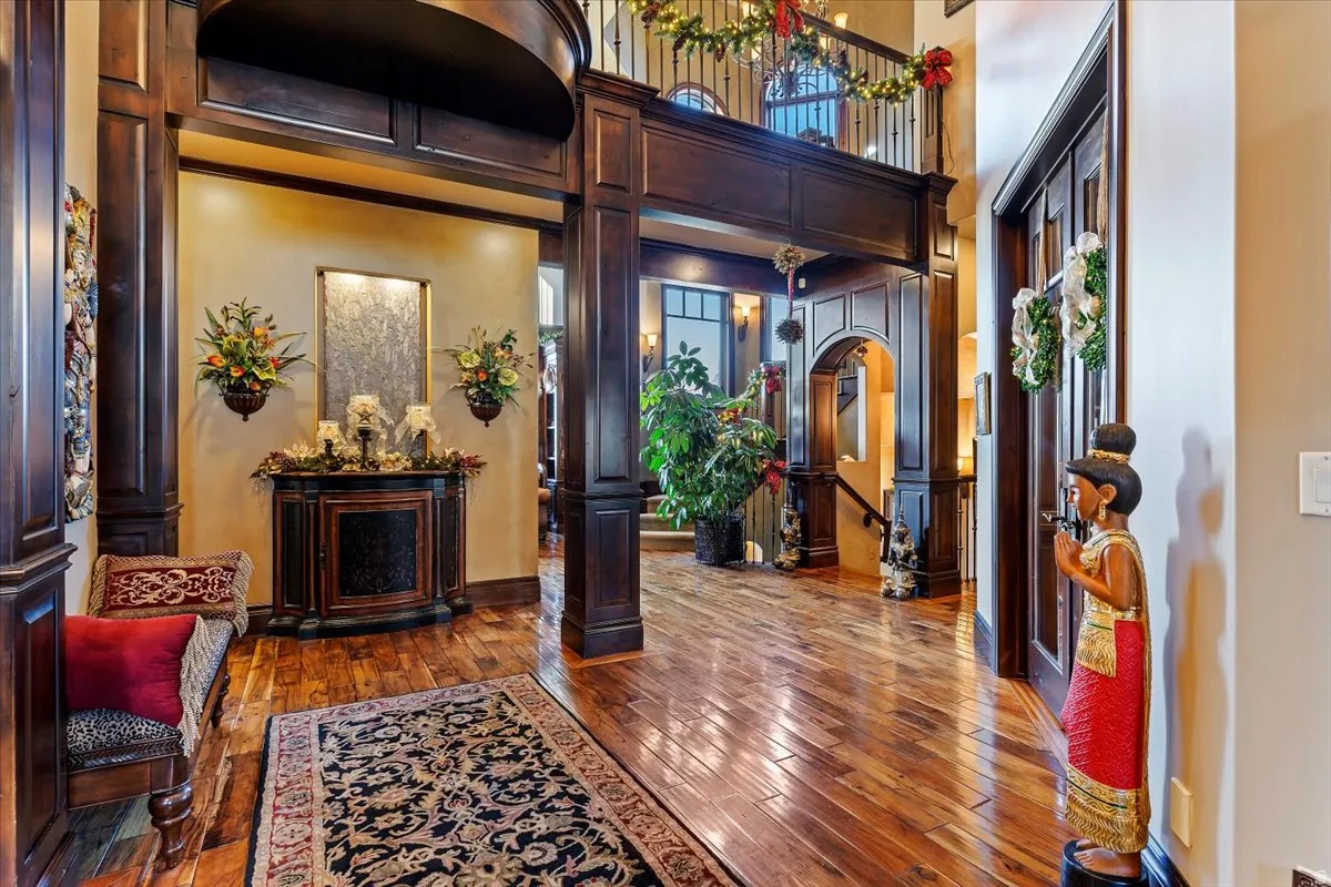 Grand entryway featuring rich Malaysian walnut wood flooring, dark wood-paneled carved archways, and a two-story ceiling with an upper-level balcony