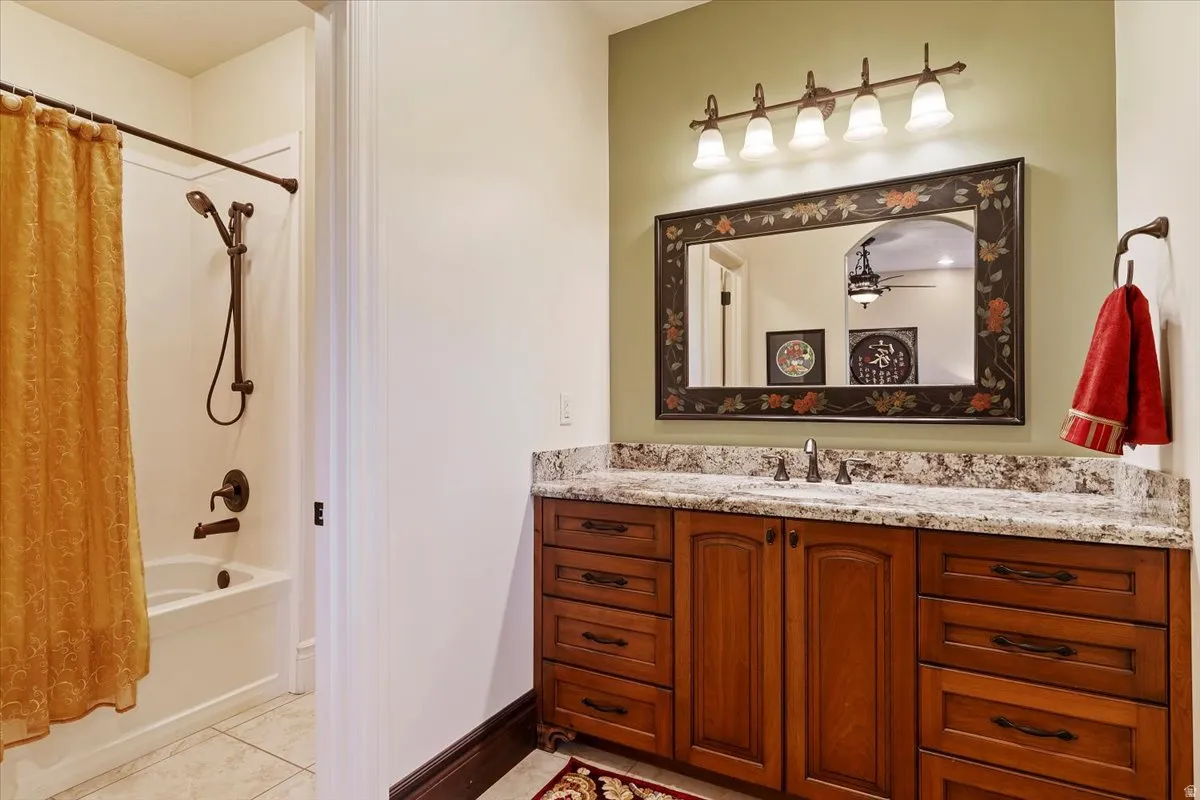 Bathroom featuring a wood-finish vanity with granite-style countertop, a decorative framed mirror, and a five-light vanity fixture