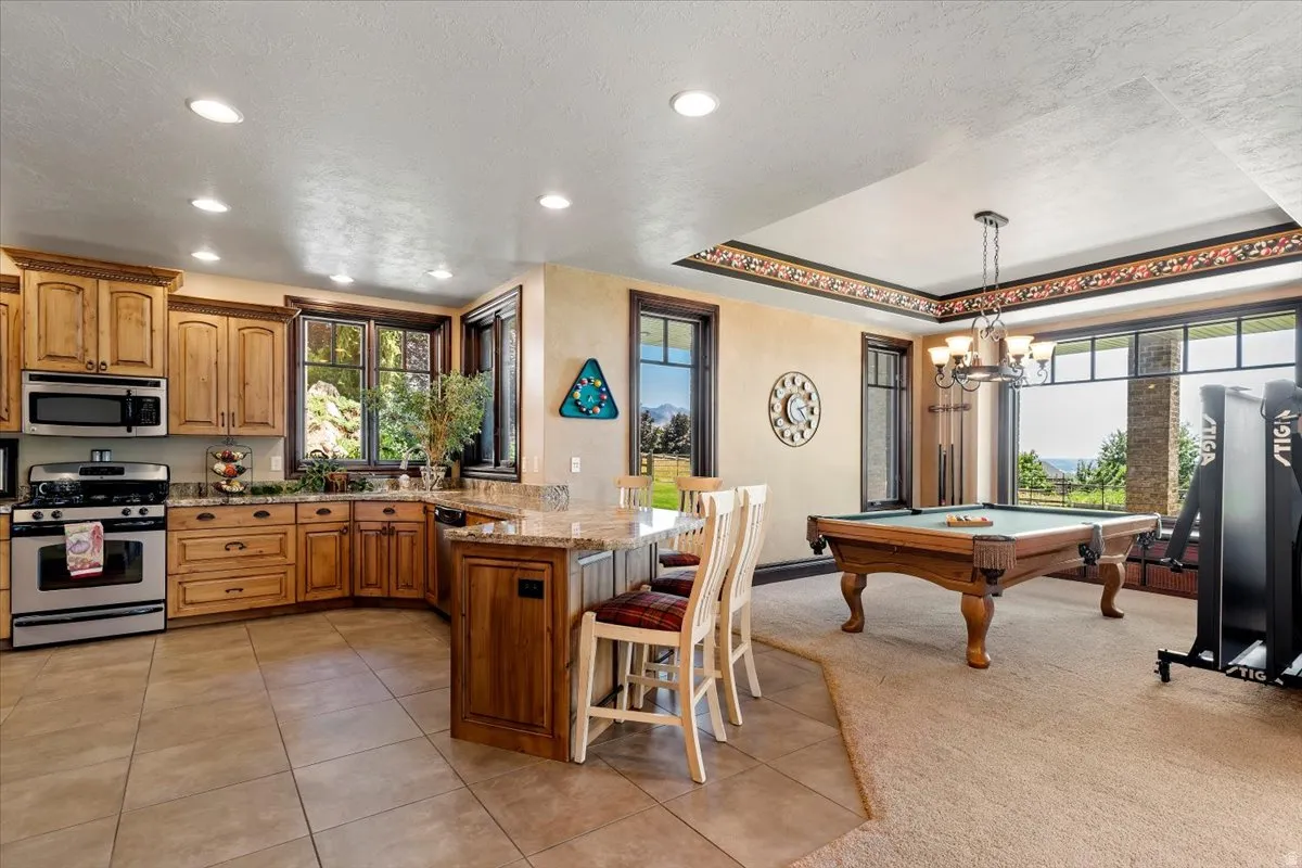 Open-concept kitchen and recreation area featuring warm wood cabinetry, stainless steel appliances, granite countertops, and tile flooring