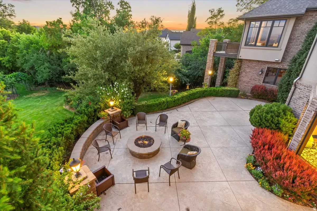 Spacious concrete patio with a built-in stone fire pit, surrounded by lush landscaping and mature trees