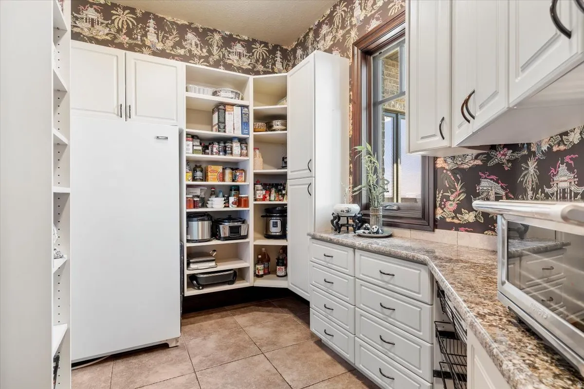 Walk through swinging doors from kitchen to a full butler pantry  featuring extensive white cabinetry, a built-in refrigerator, corner shelving,  drawers, and a window with wood trim