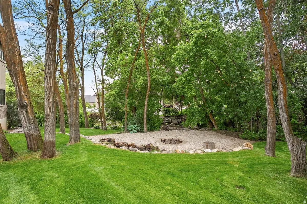 Expansive backyard featuring a manicured lawn, established trees, and a gravel fire pit area with stone edging