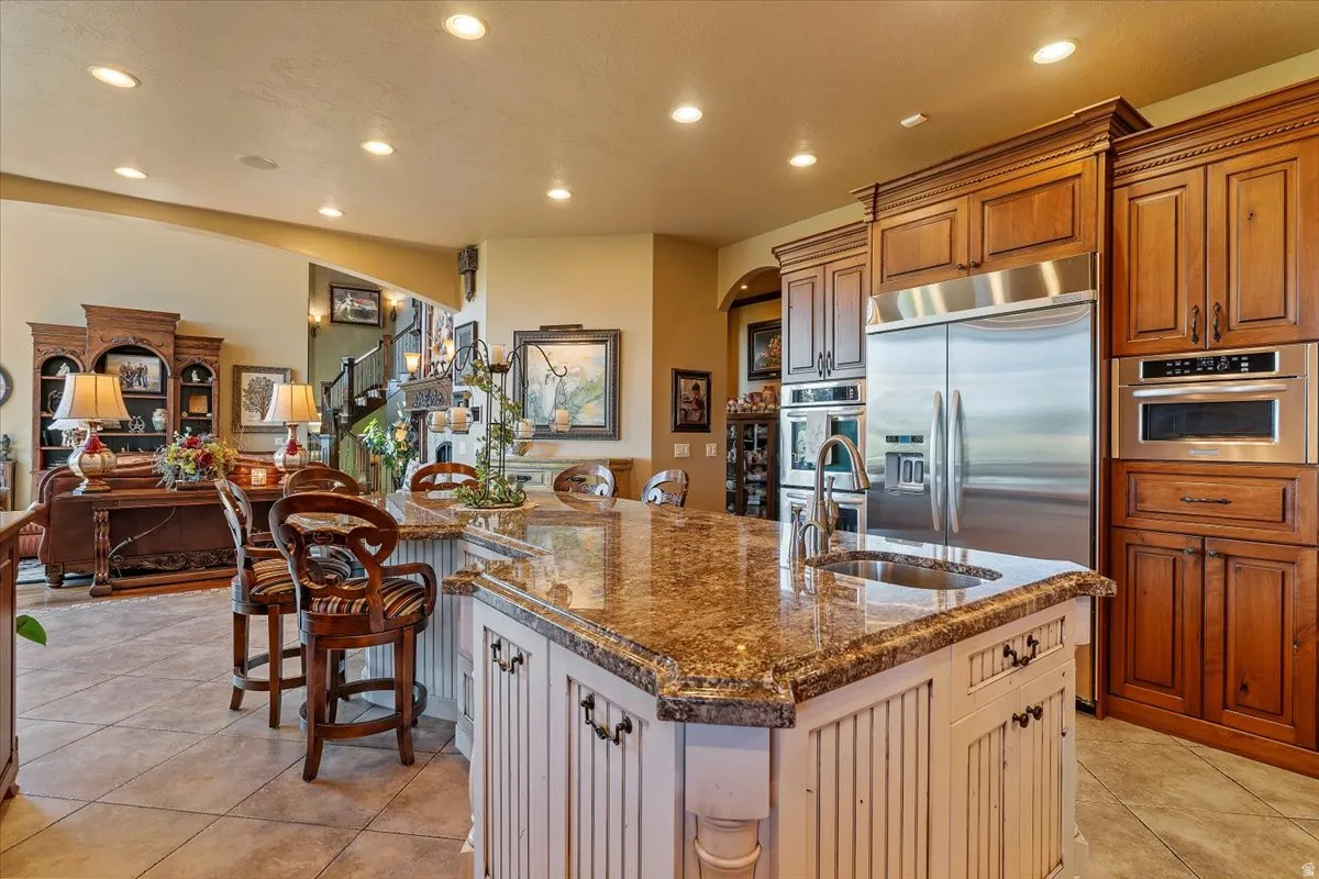 Gourmet kitchen featuring a large island with granite countertops, an undermount sink with a gooseneck faucet, and integrated stainless steel appliances including a refrigerator, wall oven, and microwave