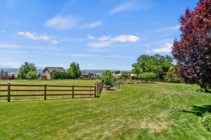 Expansive lawn area with a three-rail fence, mature trees, and landscaping, set against a distant mountain backdrop