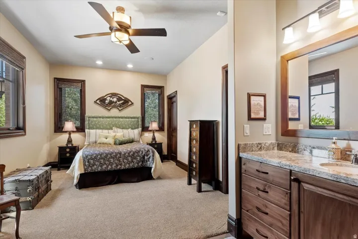 Carpeted bedroom with multiple dark-framed windows, a ceiling fan, recessed lighting, and an attached vanity featuring a granite countertop, undermount sink, and wood-finish cabinetry
