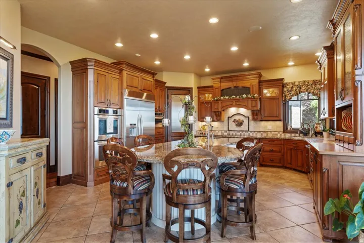 Expansive kitchen featuring an oversized island with seating, integrated stainless steel appliances, custom cabinetry, a tile backsplash, and recessed lighting