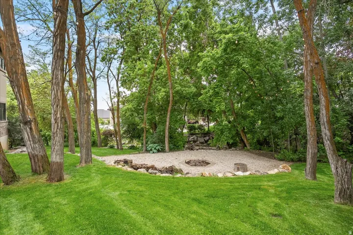 Expansive backyard featuring a manicured lawn, established trees, and a gravel fire pit area with stone edging