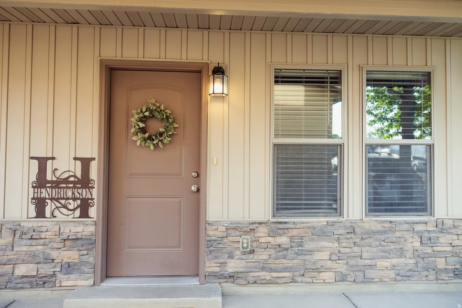 Property entrance featuring vertical siding, a paneled door, decorative exterior lighting, and stacked stone accents
