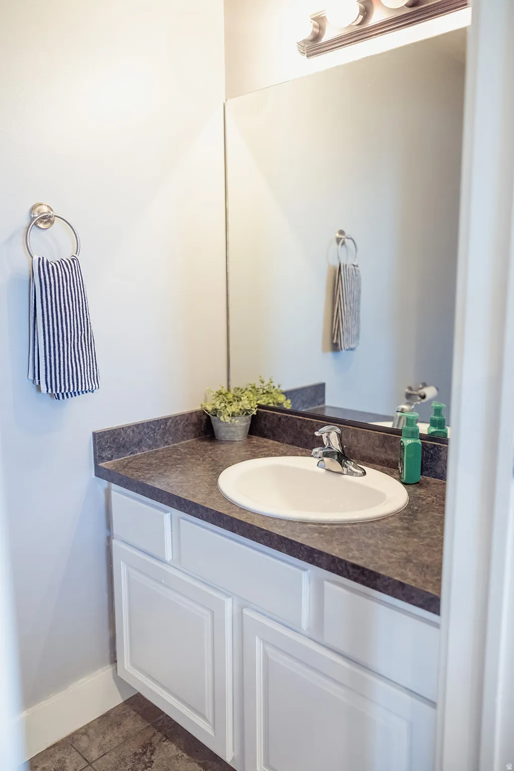 Bathroom vanity featuring a white oval undermount sink with chrome faucet, dark textured countertop, and white shaker-style cabinetry