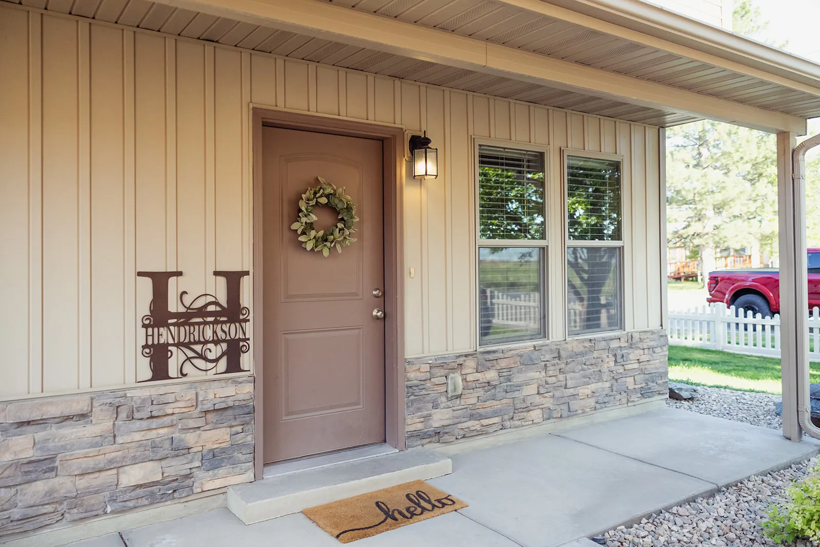 Welcoming covered porch entry featuring stone accent siding, vertical board siding, and an exterior wall lantern