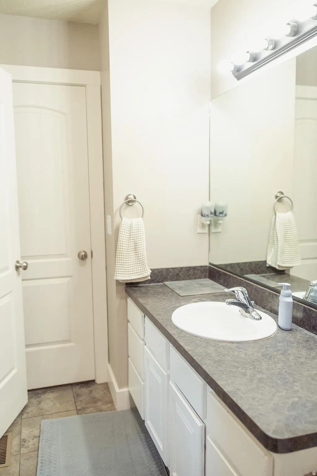 Vanity featuring a white oval undermount sink with chrome faucet, dark countertop, and white cabinetry
