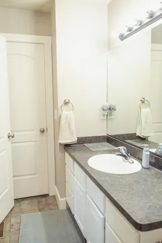 Vanity featuring a white oval undermount sink with chrome faucet, dark countertop, and white cabinetry