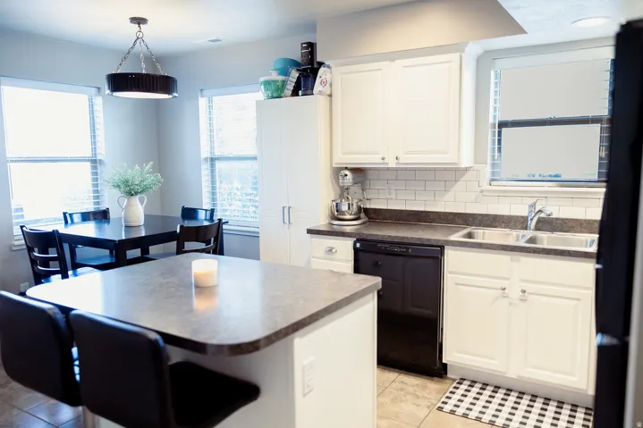 Kitchen area featuring white cabinetry, subway tile backsplash, a dual basin stainless steel sink, and a built-in dishwasher