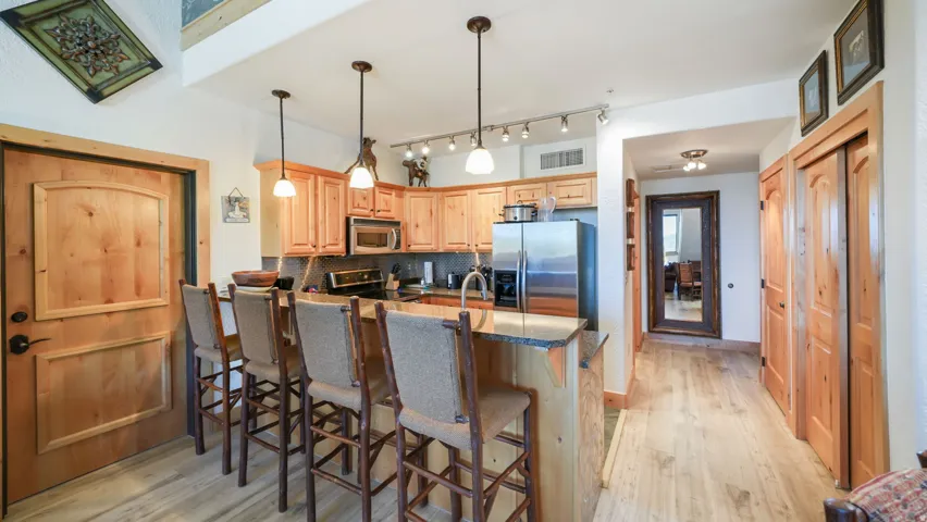 Kitchen with wood-finish flooring, natural wood cabinetry, stainless steel appliances, and a breakfast bar with pendant lighting