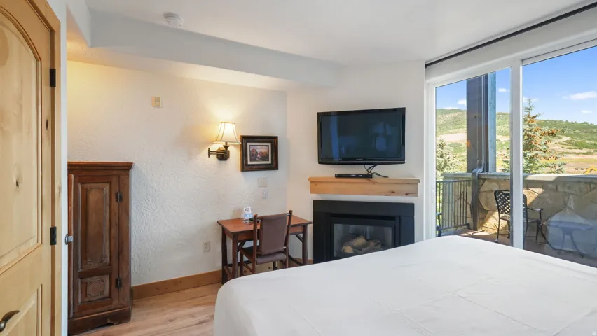 Bedroom featuring a gas fireplace with a wood mantle, a wall-mounted television, and wood-finish flooring