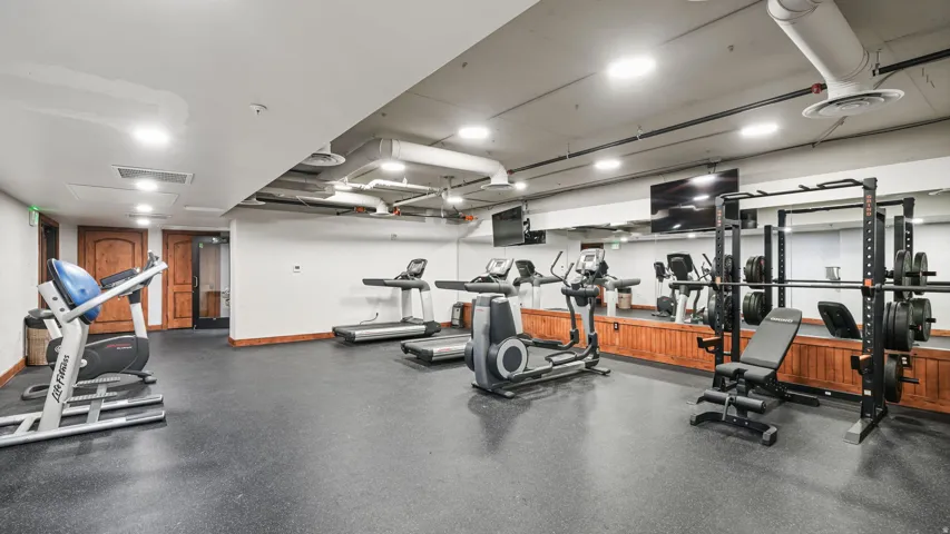 Spacious fitness center featuring rubber flooring, exposed ceiling ducts, recessed lighting, and wall-mounted mirrors