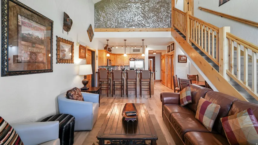 Open-concept living space with vaulted ceilings, wood-finish flooring, a wood staircase with natural wood railings, and a kitchen featuring a breakfast bar with seating