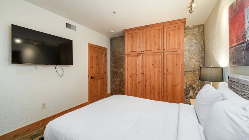 Bedroom featuring a built-in wood cabinet with multiple doors, a wood-finish door, and a wall-mounted flat-screen television