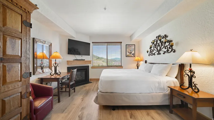 Spacious room featuring wood-finish flooring, a corner fireplace with a mantel, and a window with horizontal blinds