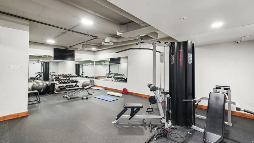 Fitness center featuring rubberized flooring, mirrored walls, exposed ductwork, a flat-screen display, and recessed lighting