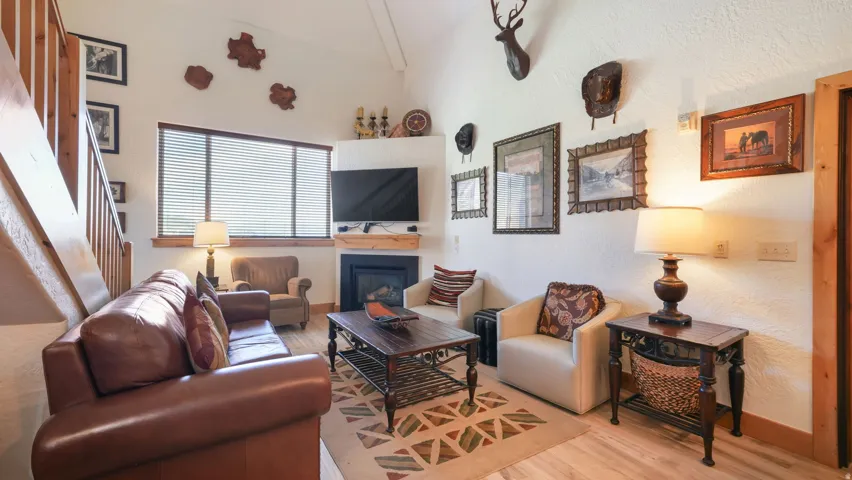 Living room featuring a corner fireplace with wood mantel, large window with blinds, and wood-finish flooring