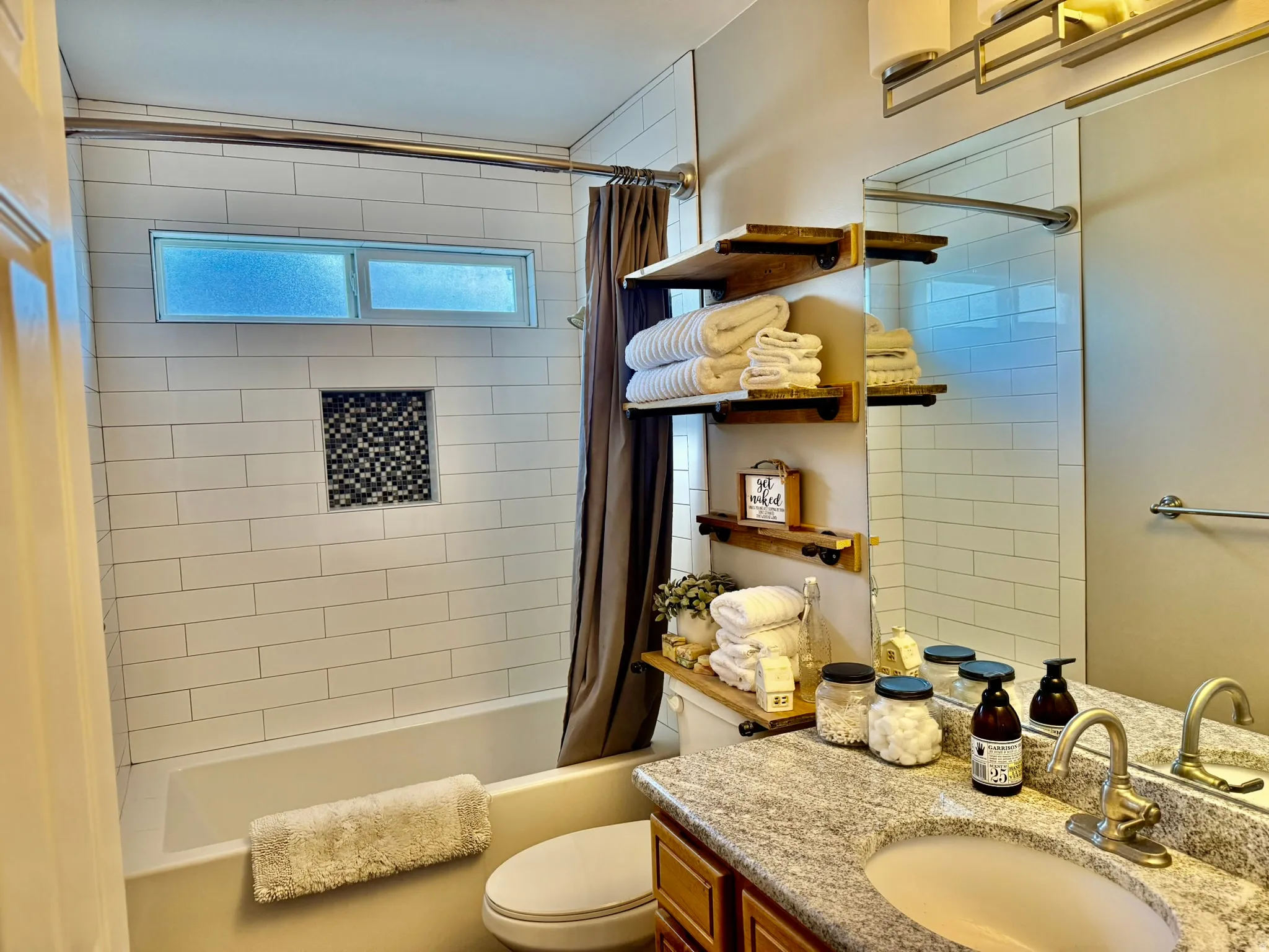 Bathroom featuring a tub and shower combination with white subway tile surround, an inset mosaic tile niche, and a horizontal window
